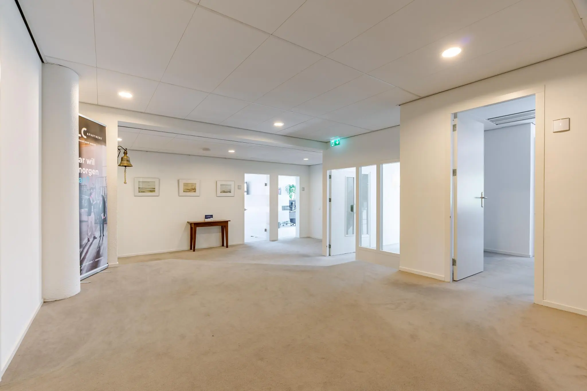 Ruime, lichte hal in een kantoorpand aan de Van Alkemadelaan met beige vloerbedekking, glazen deuren en minimalistische inrichting.